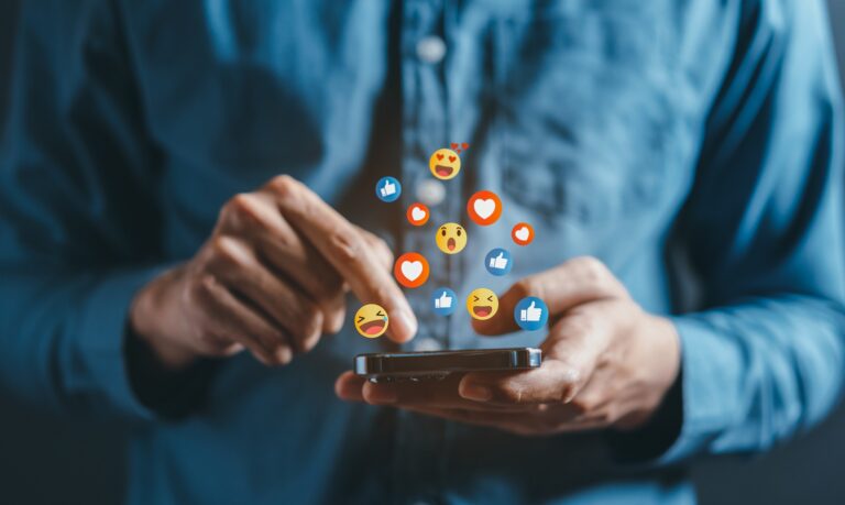 A person interacting with their cell phone with several emojis floating above the screen.