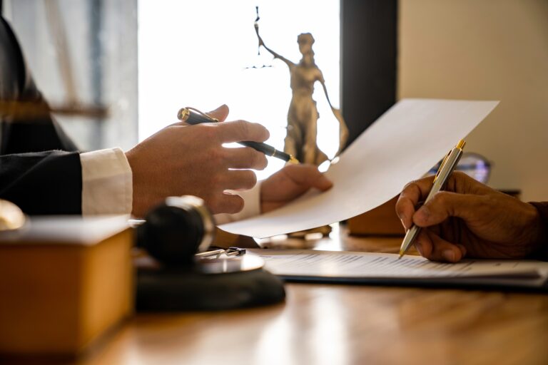 Two people at a desk reviewing paperwork in front of a gavel and scales of justice.