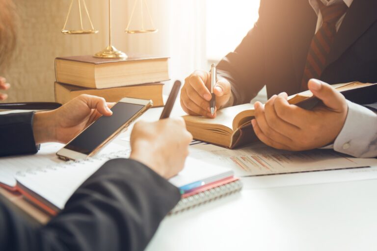 An attorney sits across from another attorney with a book and a phone in their hands.