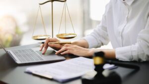 A female lawyer sitting next to a gavel and scales of justice typing on her laptop.