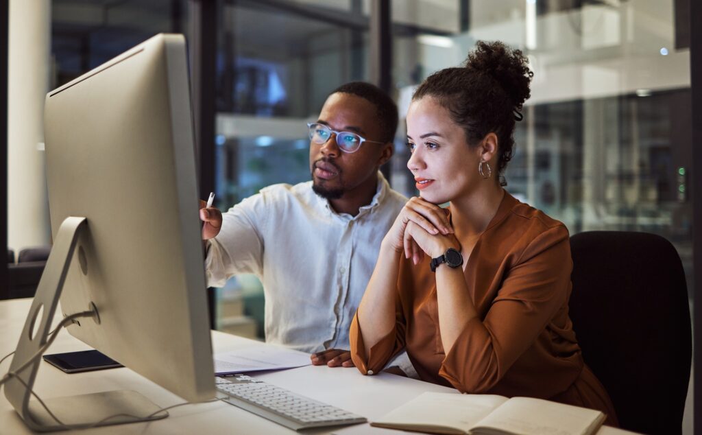 A man and woman sit at a desk behind a computer monitor discussing what they are seeing.