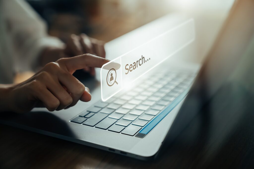 A person at a desk in front of a silver laptop pressing a floating representation of a search box.