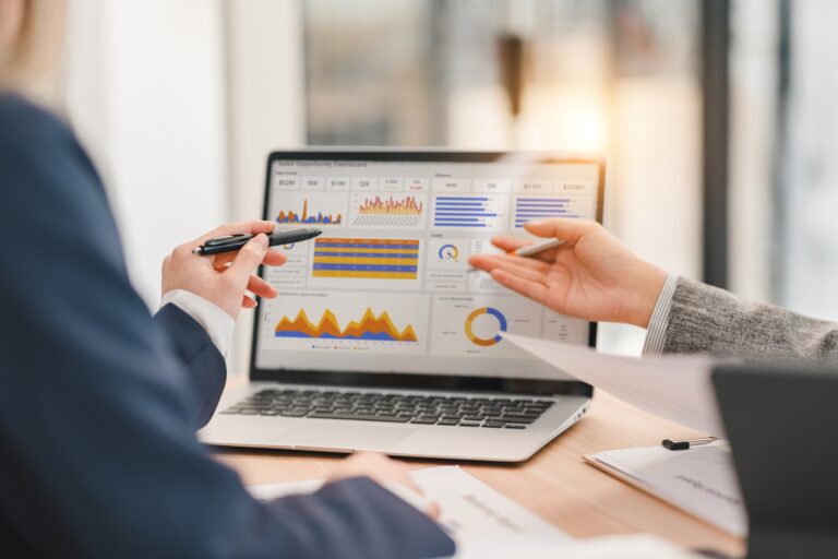 Two attorneys look at statistics on a laptop sitting on a desk.