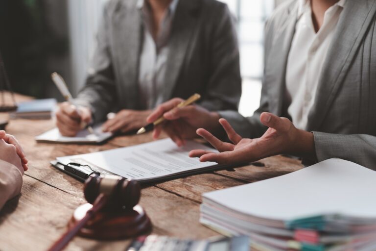 Two female attorneys in grey business suits sitting at a desk in front of paperwork and a gavel.