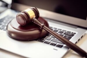 A brown wooden gavel resting on a silver laptop's keyboard on a desk.