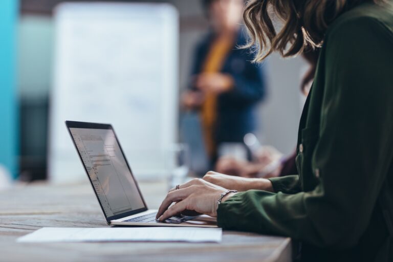 A woman looks down at a laptop while her hands rest on the keyboard sitting at a desk.