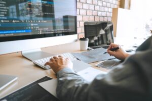 A man sits behind a desk at a computer designing a website.