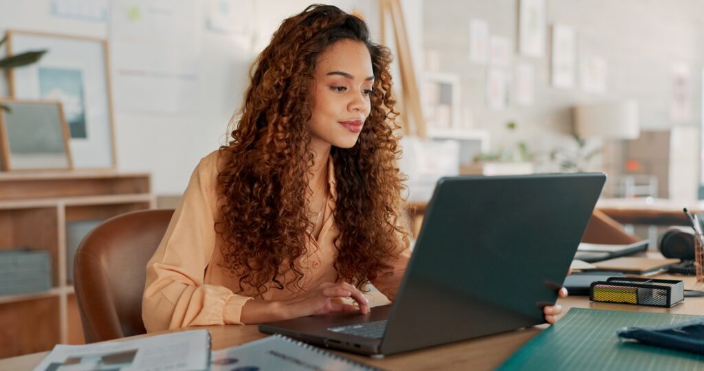 A person sitting behind a laptop with a slight smile while they type on the keyboard sitting at a desk in an office.