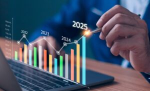 A man un front of a laptop pointing a pen at a graphic of a graph with years on it.