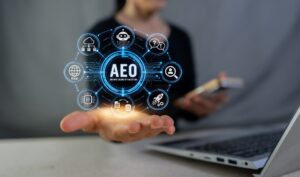 A person behind a laptop holds their hand out while a floating AEO graphic rests above it.
