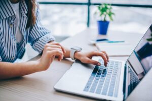 A woman sits at a desk typing on a laptop.
