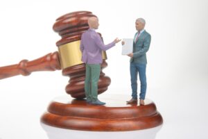 Two miniature figures depicting attorneys stand next to a gavel resting on its stand.