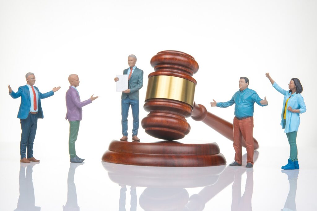 A small figurine depicting a lawyer holding paperwork in a suit sits next to a gavel on its stand near four other figures.
