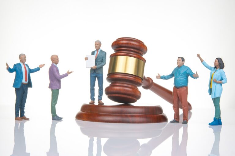 A small figurine depicting a lawyer holding paperwork in a suit sits next to a gavel on its stand near four other figures.